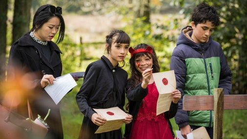 A group of four children dressed up for Halloween walk along a garden trail.